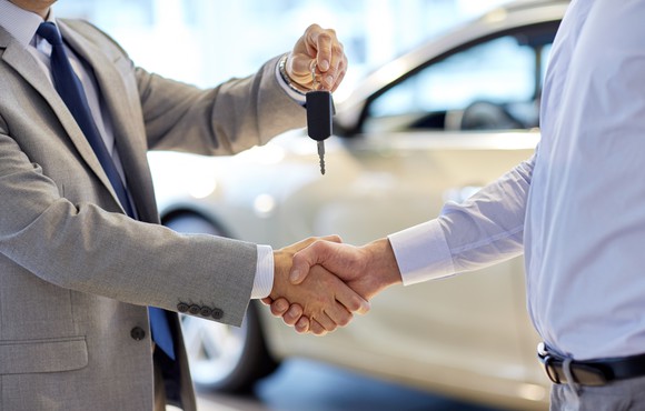 A customer shakes hands with a car salesman while receiving his car key.