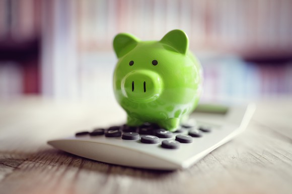 A green piggy bank sits atop a calculator on a wooden surface.