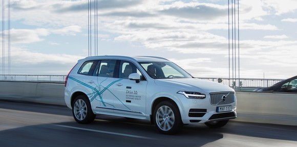 A white Volvo SUV with self-driving sensors is shown in traffic on a bridge.