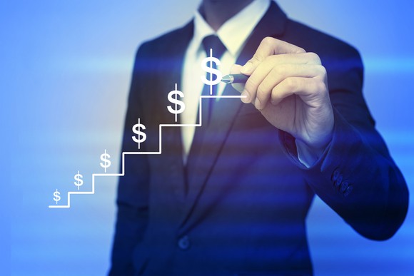 Business man holding pen up to drawing of steps with dollar symbols