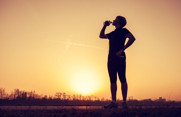 Runner stopped to drink water with sun on horizon in background