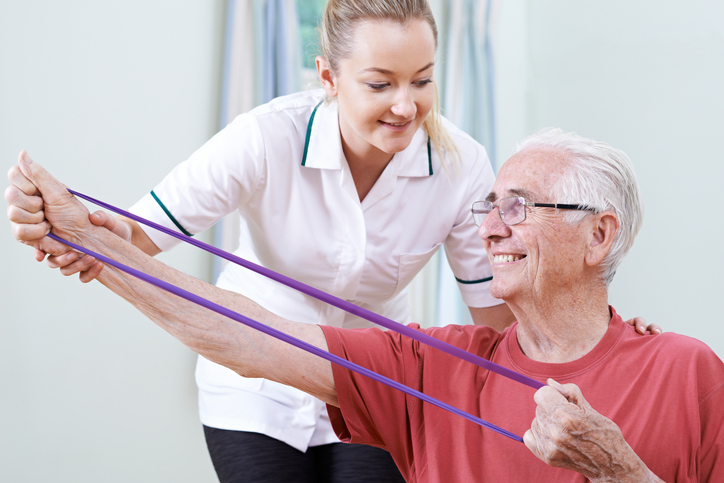 A physical therapist assists a senior with an exercise.