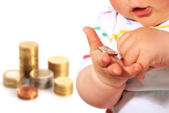 Baby holding coins, with money stacked in the background