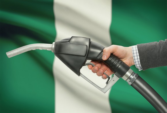A hand holding a fuel pump nozzle with the Nigerian flag in the background.