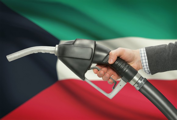 A hand holding a fuel pump with the Kuwaiti flag in the background.