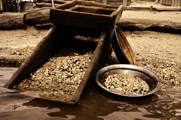 Gold panning tools full of gold, sitting on the edge of a body of water..