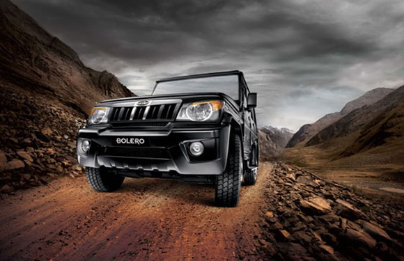 A black Mahindra Bolero, a rugged-looking SUV, on an unpaved mountain road.