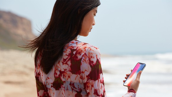 Woman looking at an iPhone 10 standing on a beach.