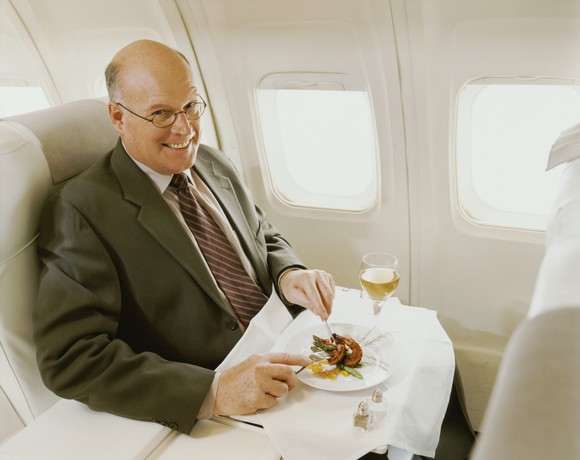 A man in a suit eating a meal aboard a plane in first class.