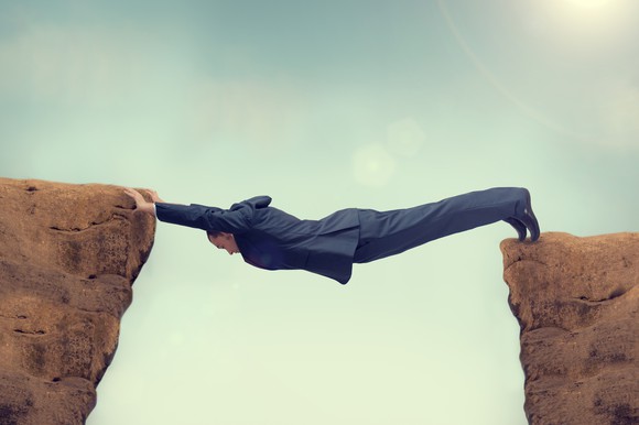 A person forms a bridge between two rock outcroppings.