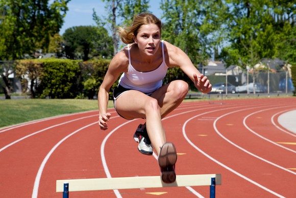 Female athlete leaping over hurdle on circular track.