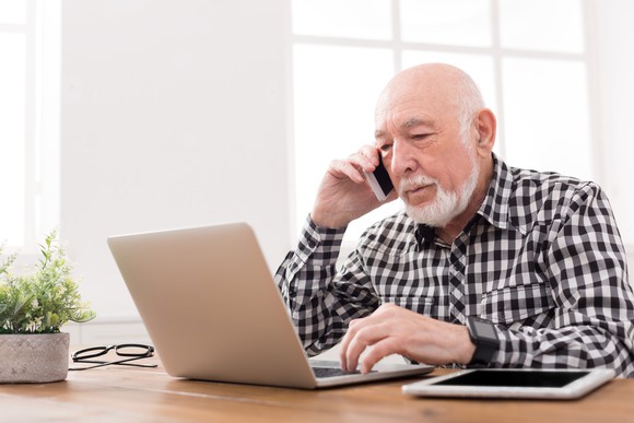 Older man on the phone while typing on a laptop