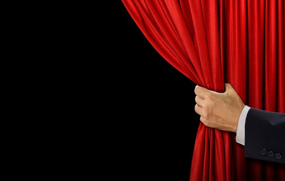 A man's arm pulls back a red curtain to reveal what's behind it.