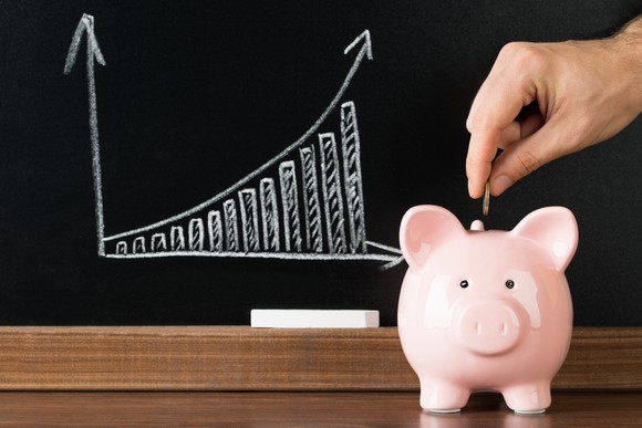 Man putting coin in a piggy bank with a chalk board showing an exponential growth chart in the background.