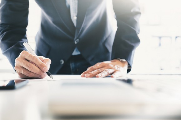 A man leans over a table with pen in hand to sign a document.