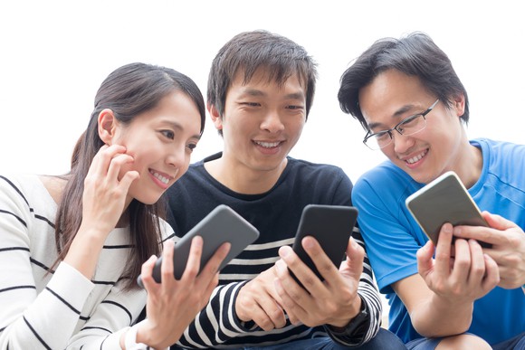 Three smiling people looking at each others smartphones.