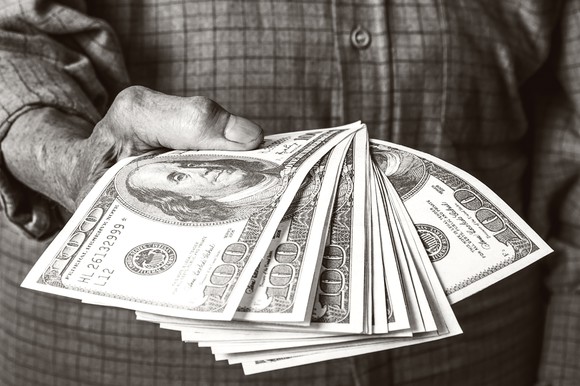 A senior holding a fanned stack of hundred dollar bills.