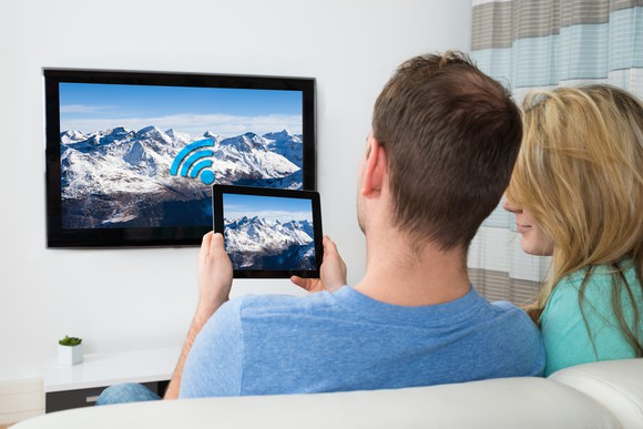 A man and woman look at a tablet in front of a television