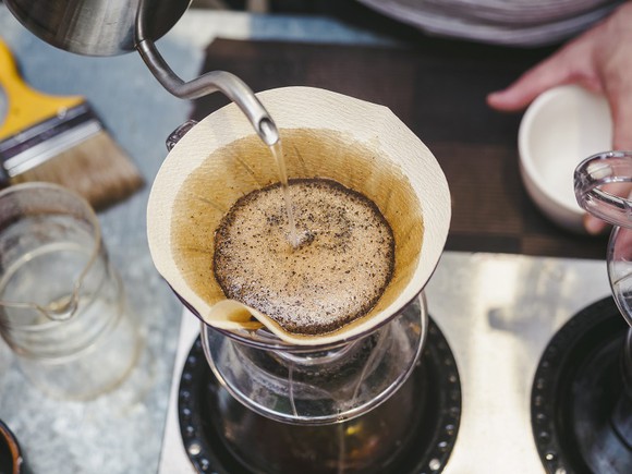 Close up of kettle spout dispensing water into a "pour-over" brewing method glass coffee carafe.