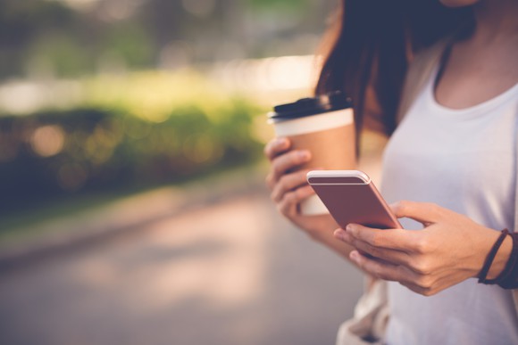 Woman using a smartphone while walking and holding a coffee