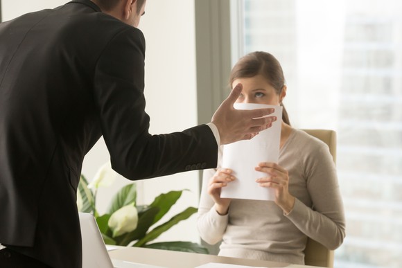 Man hovering over a woman covering her face with a piece of paper