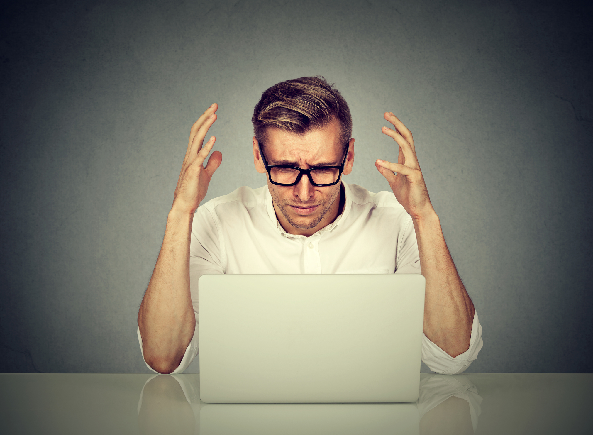 A man throws up his hands while looking at a laptop computer.