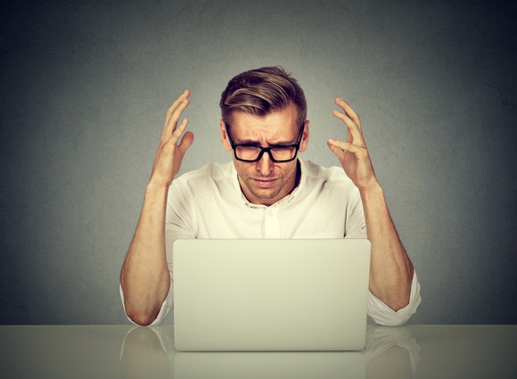 A man throws up his hands while looking at a laptop computer.