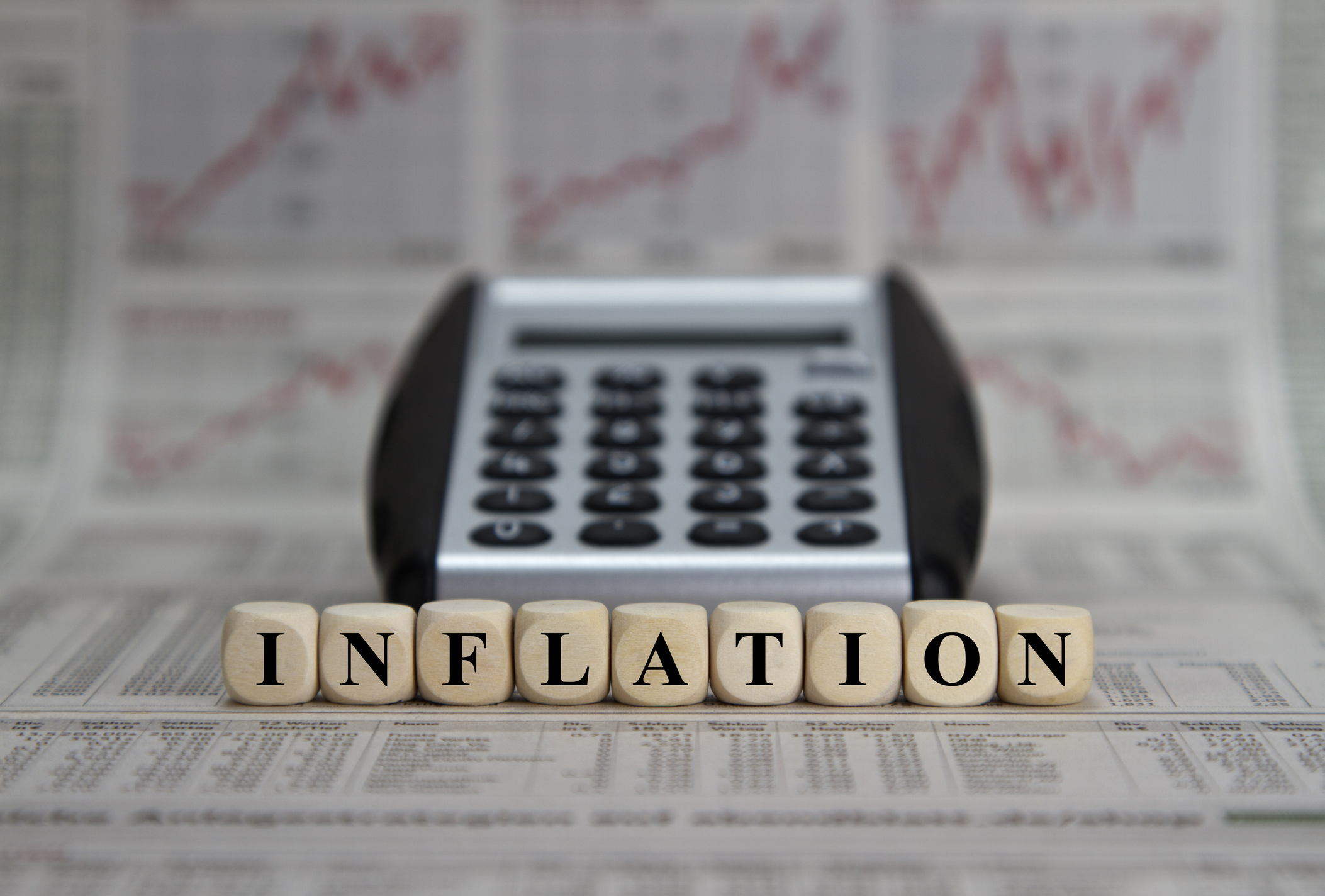 The word "inflation" spelled out with dice in front of a calculator and various rising charts in a newspaper.