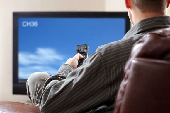 A man watches television while holding a remote.