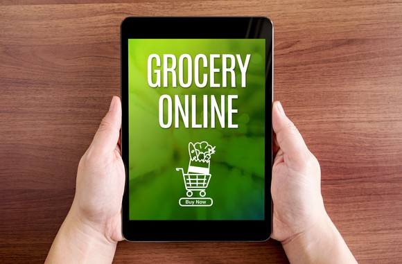 Two hands hold a tablet showing the words "grocery online" and a graphic of a filled shopping cart.