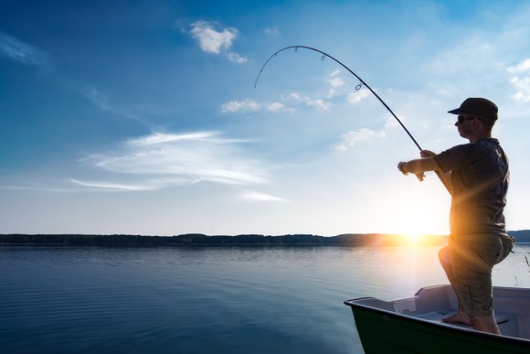 A man reels in his fishing line as the sun sets in the background.