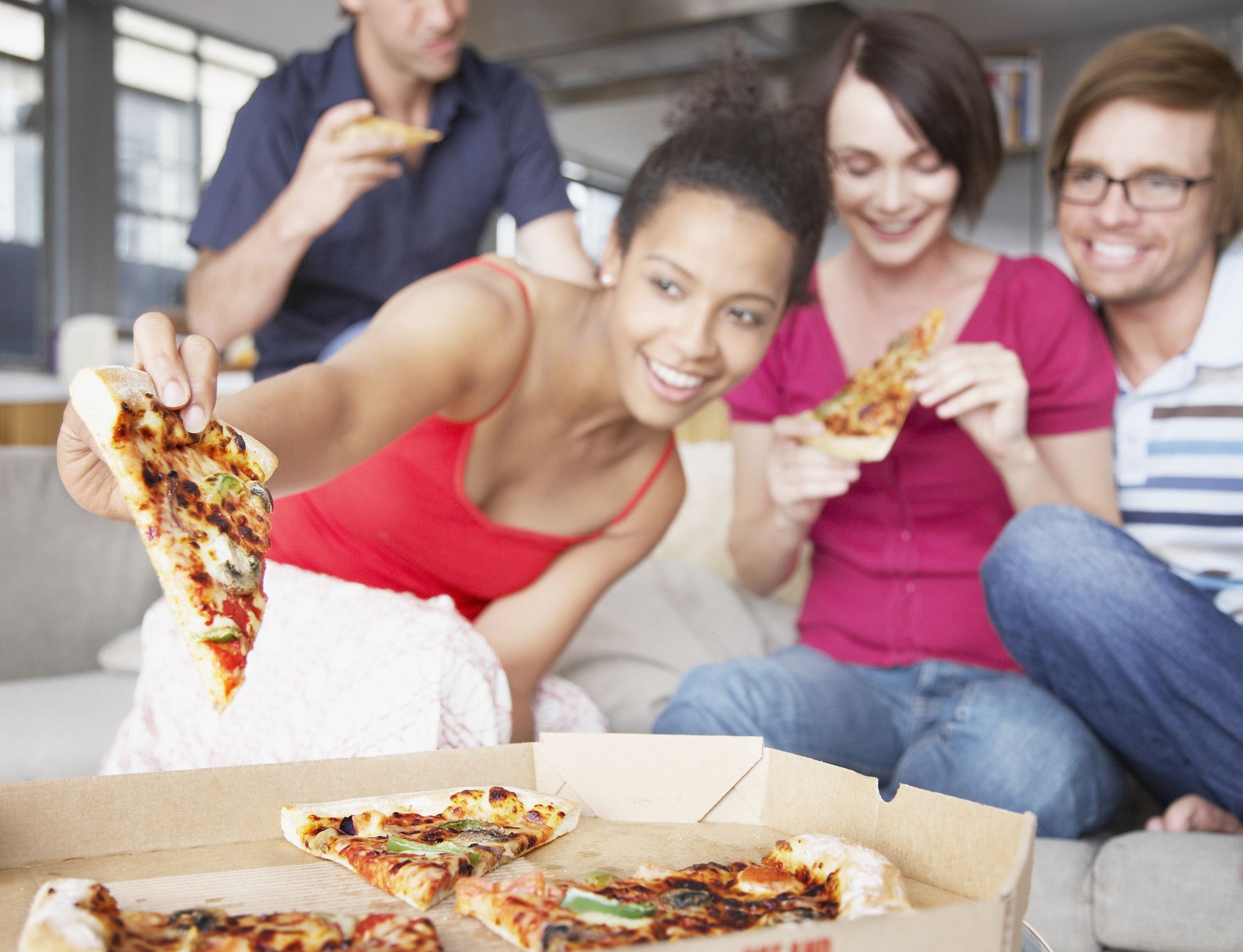 Four friends sharing pizza on a couch.