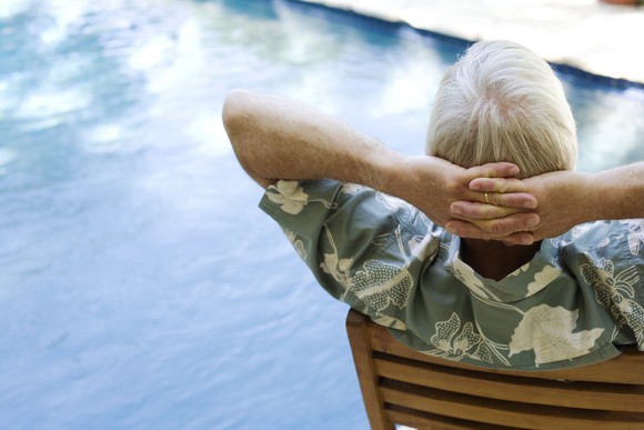 An elderly man relaxes by a pool.