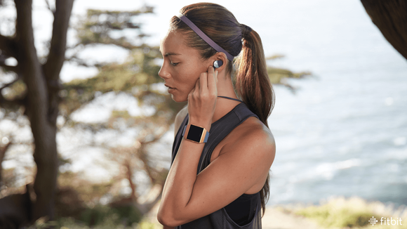 A jogger wearing an Ionic smartwatch and Fitbit Flyer headphones.