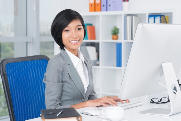 A woman typing on a desktop computer and smiling