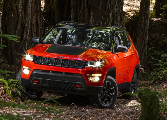 A bright red 2017 Jeep Compass, a compact SUV, on a trail in the woods.