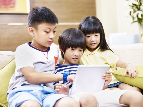 Asian brothers and sister staring at a tablet.