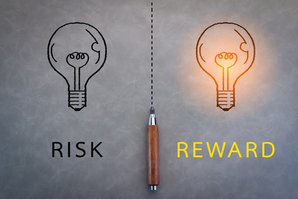 Drawing of two light bulbs separated by a dotted line with an ink pen. "Risk" is written under one bulb while "reward" is written beneath the other, which is lit up.