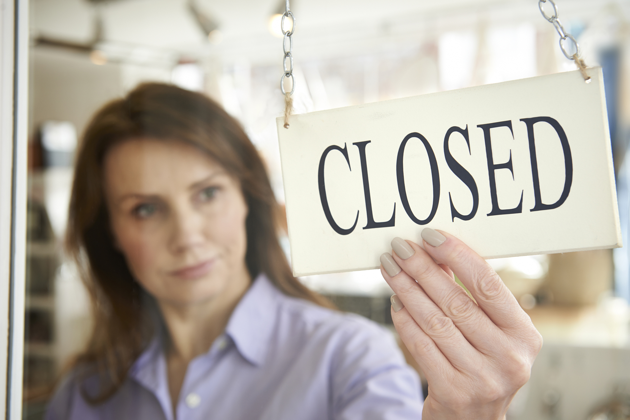 A woman turning a sign to closed in her place of business.