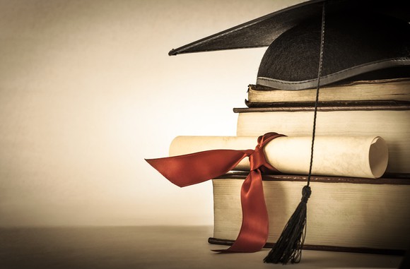 A graduation cap and a rolled-up diploma on a stack of books.
