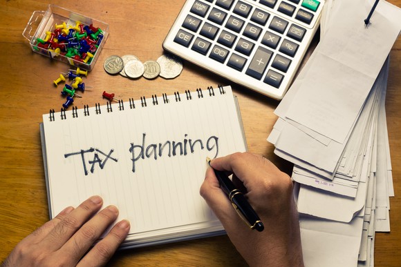 "Tax planning" written on notebook with calculator, receipts, and coins on a desk. "Tax planning" written on notebook with calculator, receipts, and coins on a desk.