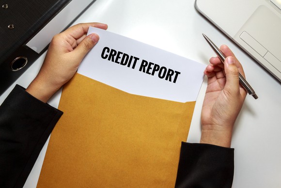 Person opening an envelope with papers titled "Credit Report"