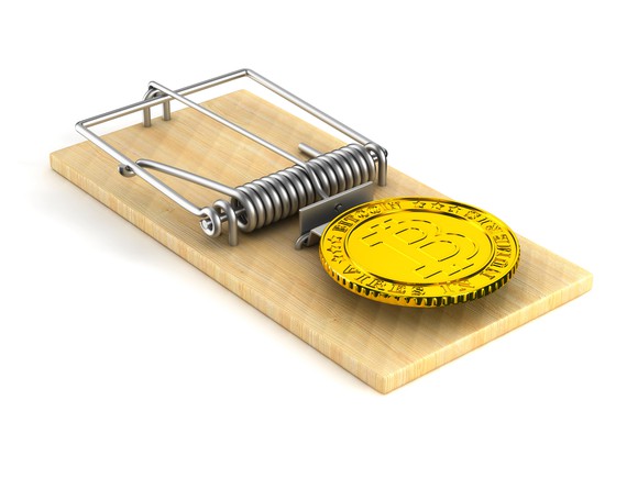 A gold physical bitcoin placed at the end of a mouse trap.