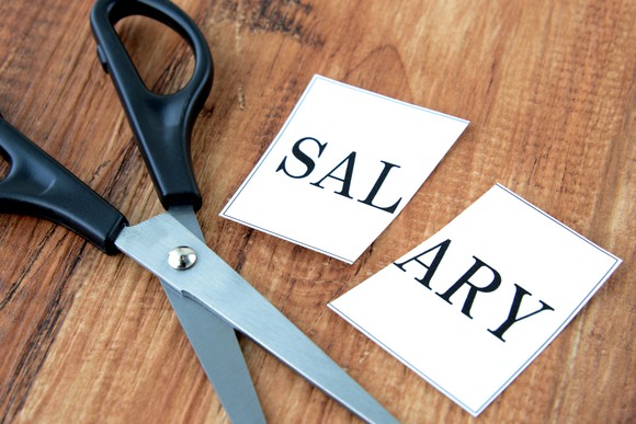 Piece of paper with the word "salary" cut in half next to an open pair of scissors