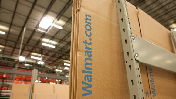 Flat-packed cardboard boxes with "Walmart.com" printed on them sitting in a warehouse.