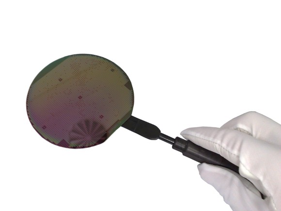 A technician holds up an unfinished semiconductor wafer on a vacuum holder.