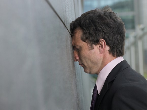 Business man leans his head against the wall.