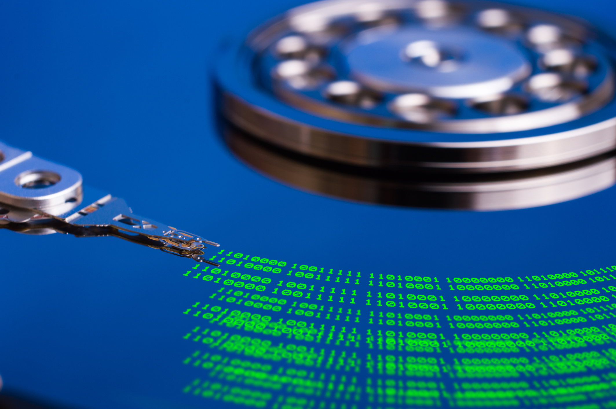 A case-less hard drive platter, showing the read/write head leaving a green trail of ones and zeroes on the disk platter.