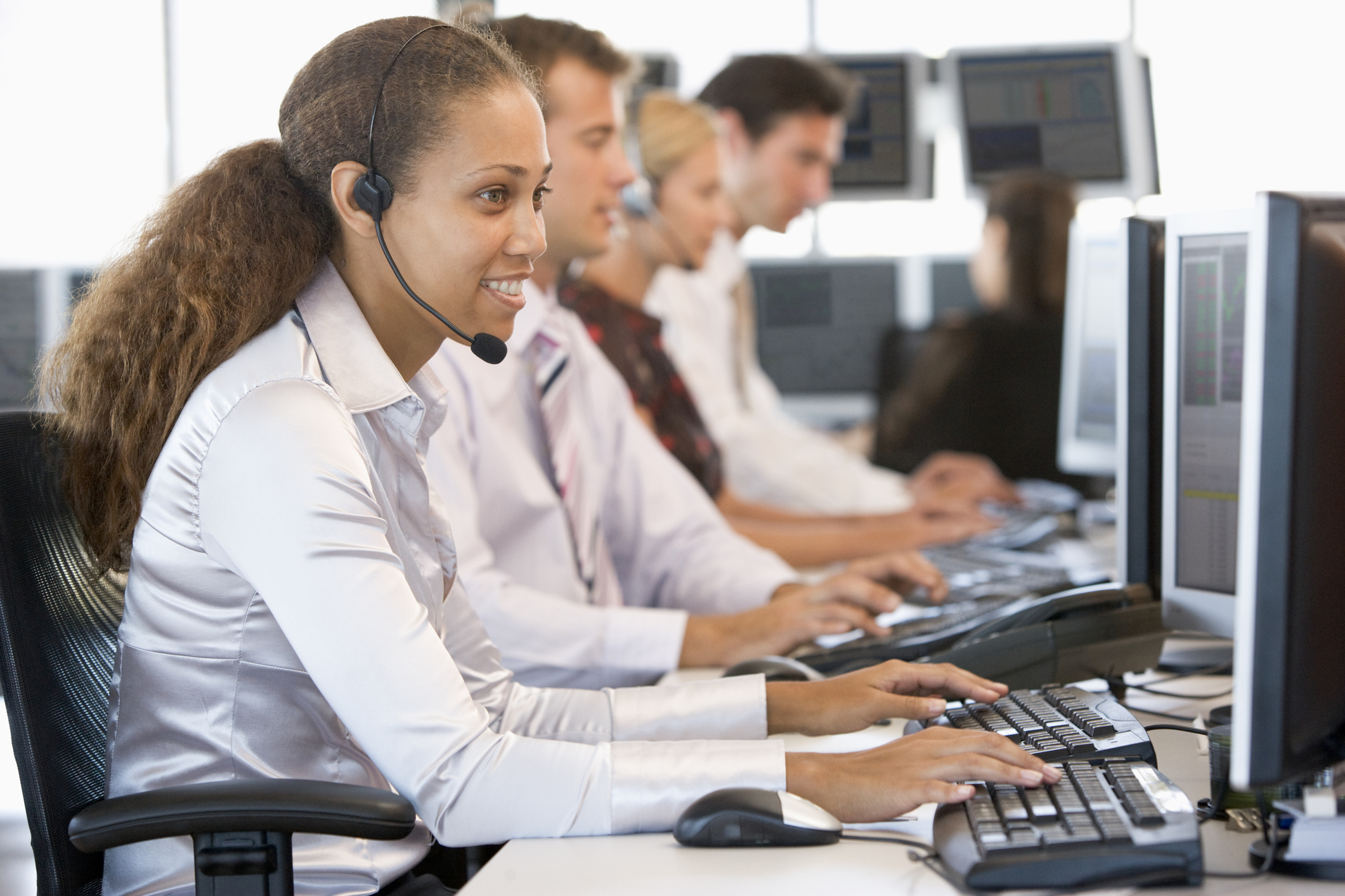 young professionals sitting at computers taking phone calls on headsets
