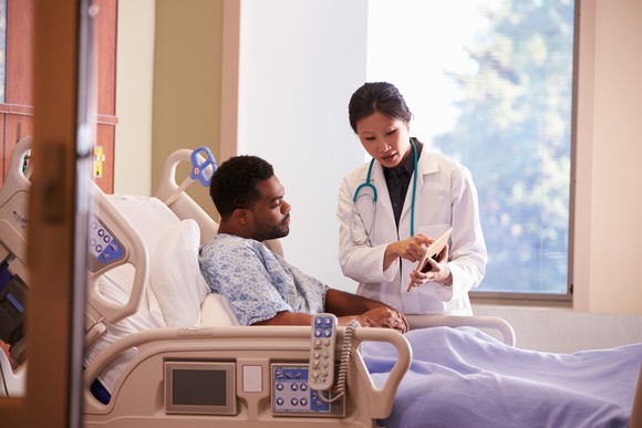 A female doctor consulting with a male patient in a hospital bed.